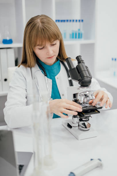 A focused image of a female scientist in a white lab coat carefully adjusting a microscope in a laboratory setting. The background includes test tubes and scientific equipment, enhancing the professional atmosphere of research and discovery. High quality photo una imagen enfocada de una científica con una bata blanca de laboratorio ajustando cuidadosamente un microscopio en un entorno de laboratorio. el fondo incluye tubos de ensayo y equipos científicos, lo que mejora la atmósfera profesional de investigaci�
