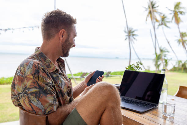 istock Man in Tropical Location Working on Laptop with Phone 2191770024