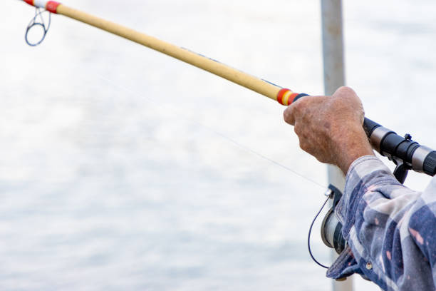 A man's hand holding a fishing rod above the water.