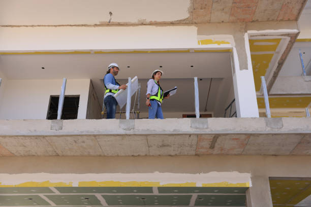istock House construction. Architects working on the project.Man and Woman with hard hats and PPE vests discussing plans with blueprints on the floor level of a construction site  looking up 2191771054