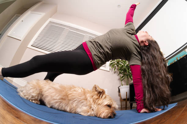 Woman doing difficult yoga pose at home while her dog sleeps under her