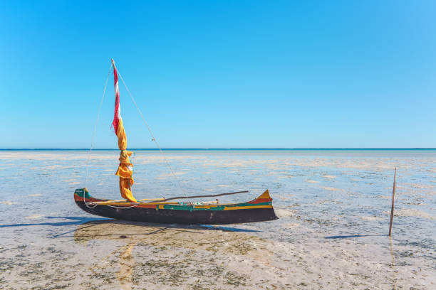 Fisherman piroga (small fishing boat with sail) waiting at the low tide coast on sunny day