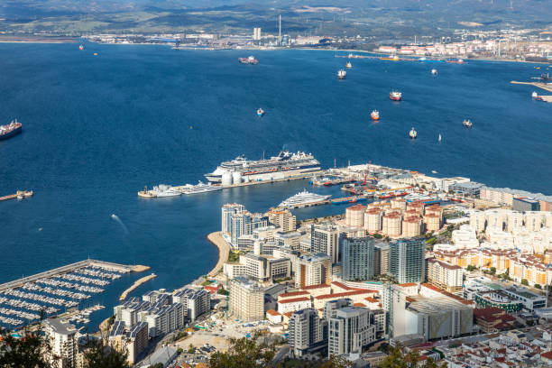 Elevated view of Westside, Gibraltar, including the cruise ferry terminal, at which is berthed a cruise whip and two private luxury yaughts. A megayacht is berthed at the Peninsula Yacht terminal. Bottom, left is the north part of Mid-Harbour Marina. In the bckground, several commercial vessels can be seen in the Bay of Gibraltar heading for the Gibraltar-San Roque oil terminal or the Endesa Port authority terminal in Algeciras, both in Spain.
