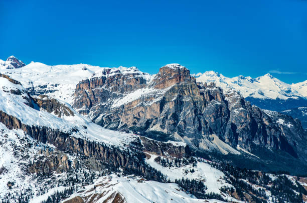 Ski area in Arabba ski resort in Dolomites, Italy, in winter. Ski slopes, pistes and lifts between rocks and trees. Part of Sella Group mountain massif in the background. Blue sky with copy space