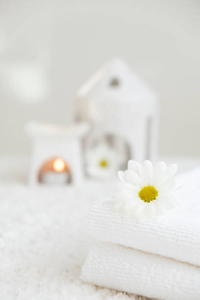 White towels with chamomile flower and aroma lamp, candle on background. Spa therapy, massage salon, romantic relaxation concept. Body care and treatment. Selflove. Copy space.