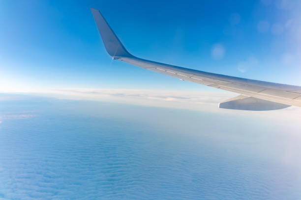 View from the airplane window at a beautiful cloudy sky and the airplane wing. Earth and sky as seen through window of an airplane.