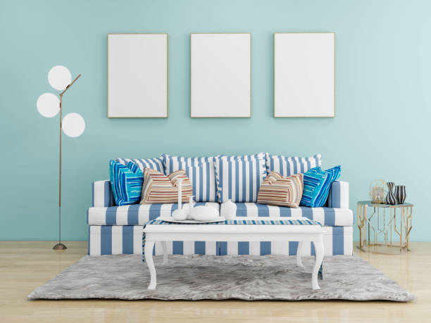istock A modern living room with a blue and white striped sofa, colorful pillows, a white coffee table, a floor lamp, and three blank frames on a light blue wall. Living room mockup template. 2191825833