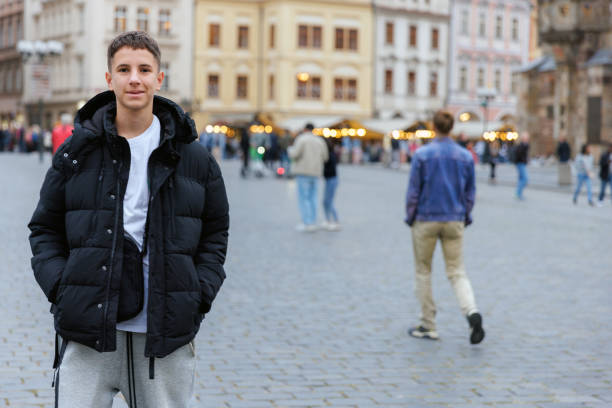 Teenage boy exploring European city of Prague, standing on stone paved square and looking at camera, gen Z and youth culture