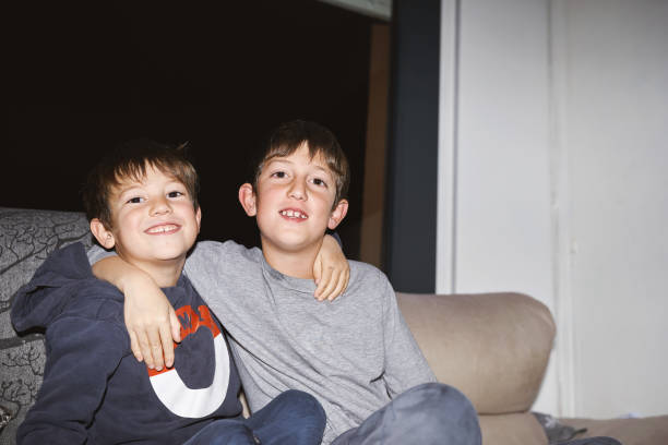 Two smiling boys sitting together on a couch, embracing and looking at the camera
