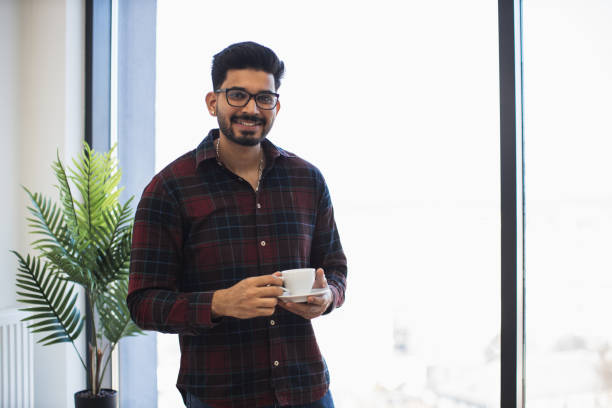 istock Young Indian man enjoying coffee in bright modern office space 2191828035
