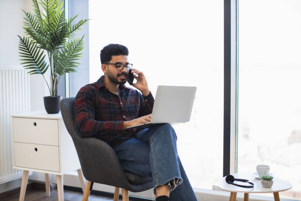 istock Indian man working remotely with laptop and phone at home office 2191828127