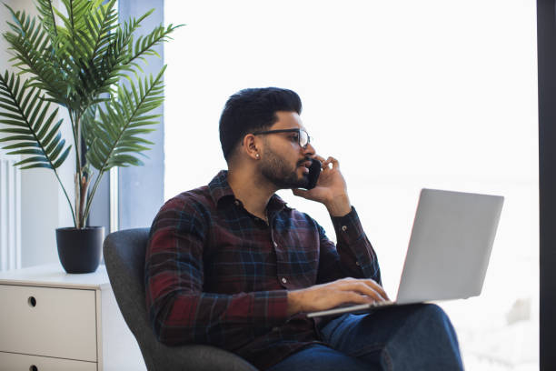 istock Indian man working remotely with laptop and phone at home office 2191828137