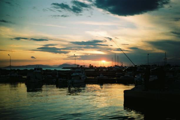 Tranquil scene of a harbor at sunset, with moored boats silhouetted against the colorful sky