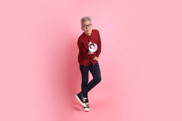 Happy Chinese New Year, asian senior man in formal and casual red shirts with gesture of shouting, holding megaphone isolated on pink background.