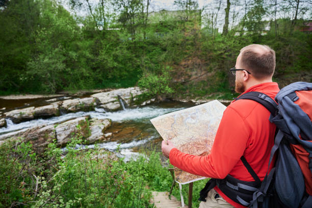 istock Bearded tourist man studies map while on wooden staircase by river. 2191850196