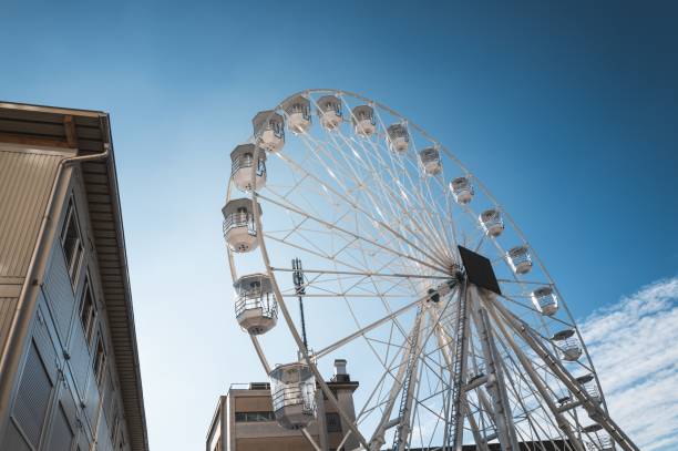 A Ferris wheel against a bright blue sky, next to a modern building, capturing urban amusement park vibes.