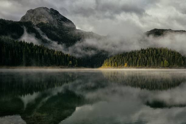 istock Misty mountain landscape with forest reflection on a tranquil lake under a cloudy sky. 2191857145