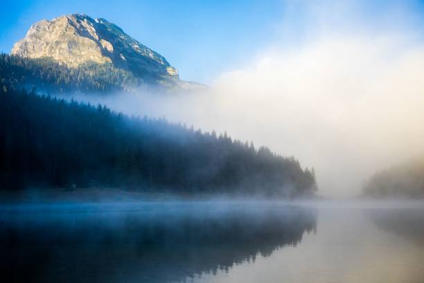 istock Misty mountain landscape with a serene lake and pine forest under a clear blue sky. 2191857146