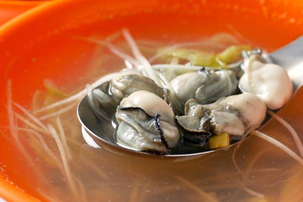 Spoonful of fresh oysters in clear soup.