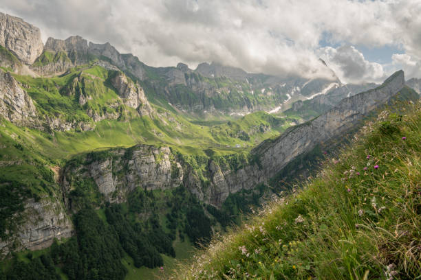 Impressive Alpstein mountains during cloudy summer day. deep valley with forest and green alpine meadow. Meglisalp mountain hut in the distance. High impressive mountain peaks, beautiful hiking area.