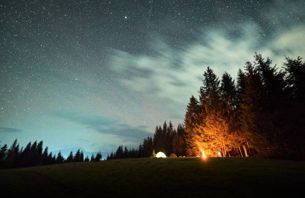 istock Campfire glows warmly beside several illuminated tents on grassy clearing under star-filled sky. 2191868166