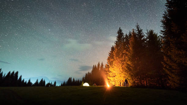 istock Campfire glows warmly beside several illuminated tents on grassy clearing under star-filled sky. 2191868167