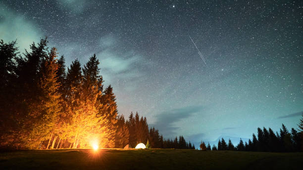 istock Campfire glows warmly beside several illuminated tents on grassy clearing under star-filled sky. 2191868175