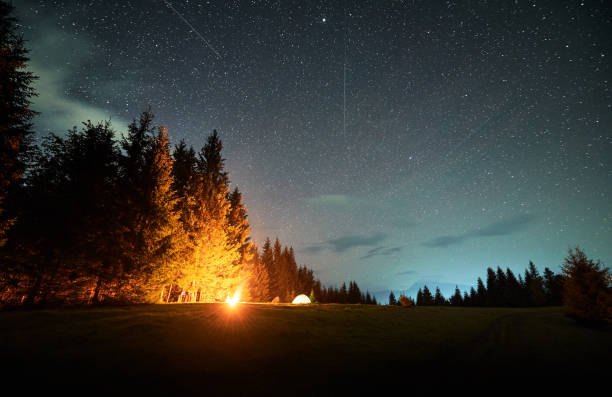 istock Campfire glows warmly beside several illuminated tents on grassy clearing under star-filled sky. 2191868182