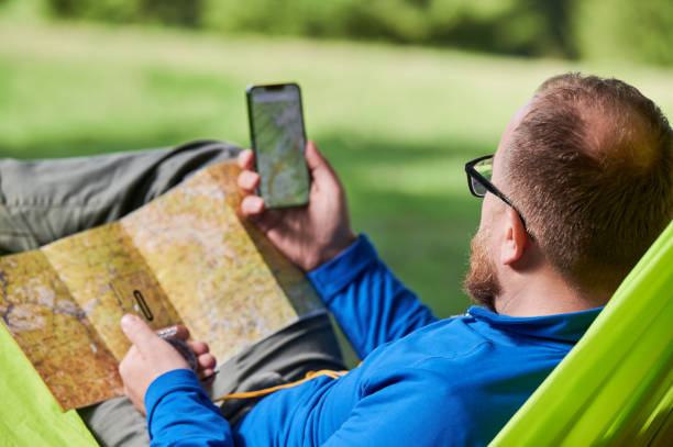 istock Man traveler studies map, checks his phone, combining traditional and modern navigation methods. 2191868220