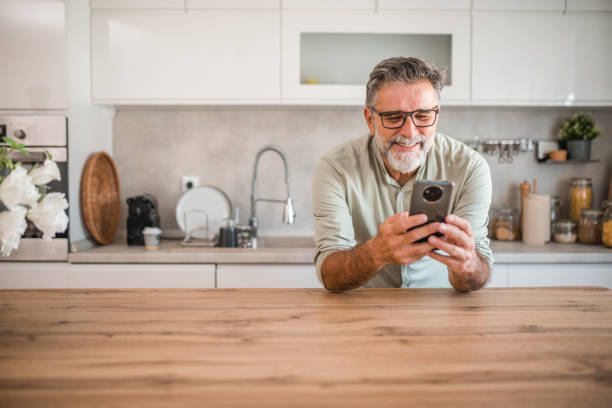 istock A carefree middle-aged man is leaning against the kitchen counter and using a mobile phone to send text messages 2191869071