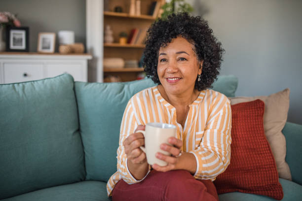 istock Portrait of smiling multiracial woman drinking coffee while sitting on comfortable sofa in living room 2191872878