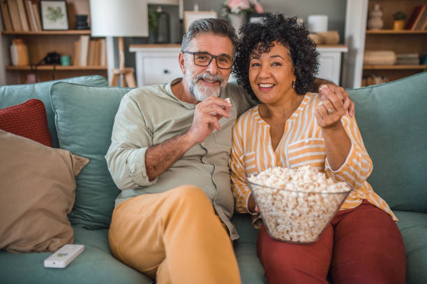 istock Smiling multiracial loving couple eating popcorn and watching TV while sitting on sofa in living room 2191872932