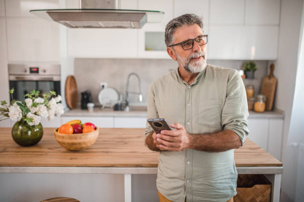 istock Waist up view of middle aged man using mobile phone in kitchen 2191872959