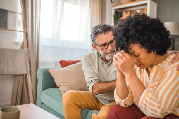 istock A woman sits in pain on the sofa, while her husband comforts her 2191873428