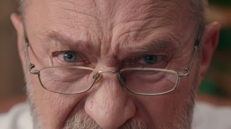 Close up cropped view angry old Caucasian man eyes male irritated glasses half face pensioner elderly businessman mature indoor looking at camera furious portrait expression annoyed headshot mad anger