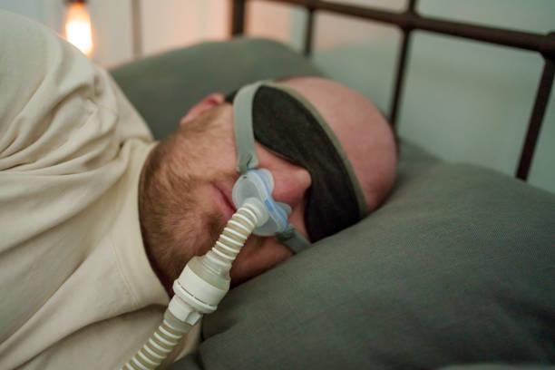 Young Man in his thirties using a sleep mask and CPAP machine to rest and sleep for therapy for Sleep Apnea