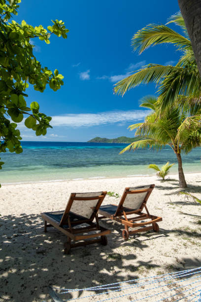 istock On a tropical island beach, brown deck chairs are set up for sunbathing, with a blue channel and distant coral as the backdrop 2191890821