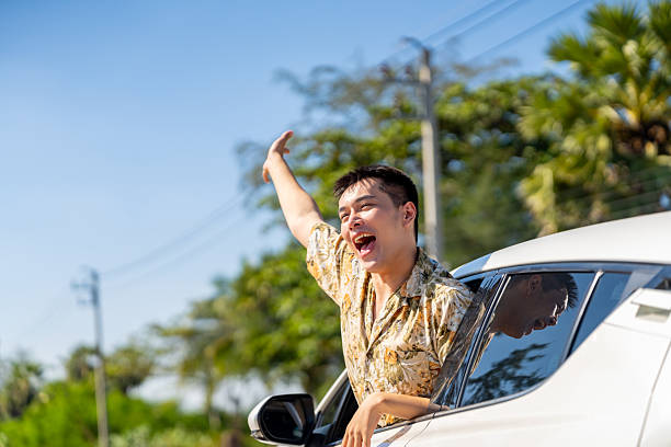 Happy people road trip travel on summer holiday vacation. Asian non binary person enjoy and fun outdoor active lifestyle travel countryside sitting in a car and looking beautiful nature out of window.