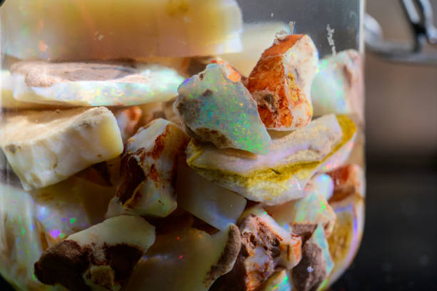 A close-up of rough opal stones in a glass container, showcasing their vibrant colors and natural textures.