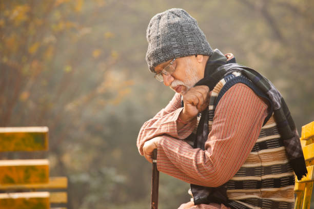 An old elegant man with walking stick sitting on bench in park on autumn day