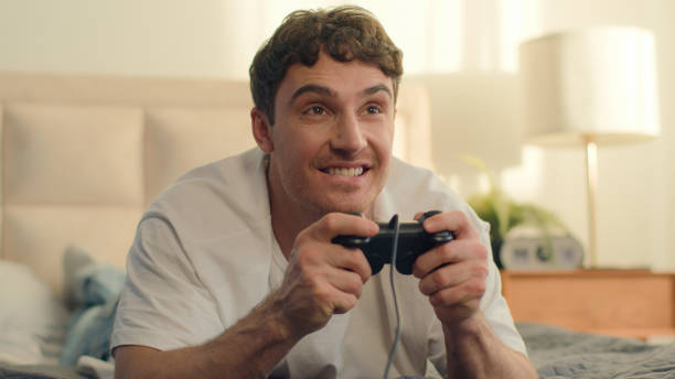 istock Playful Caucasian European young man lying on bed playing console holding joystick video games fun weekend home enjoy guy hobby leisure hands technology virtual cyberspace cheerful excitement smiling 2191914821