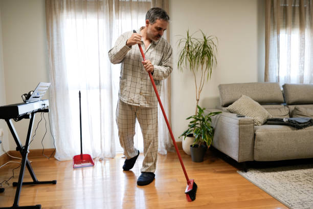 istock Man in pyjamas sweeping the floor in his living room 2191921066