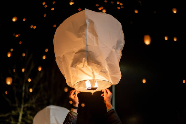 istock Person is carefully holding a large, illuminated white sky lantern, preparing to release it into the night sky where many other lanterns are already floating gently 2191921600