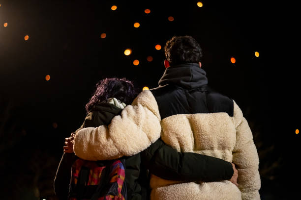 Young couple embracing while watching floating lanterns illuminate the night sky, sharing hopes and dreams for the future in a moment filled with love and connection