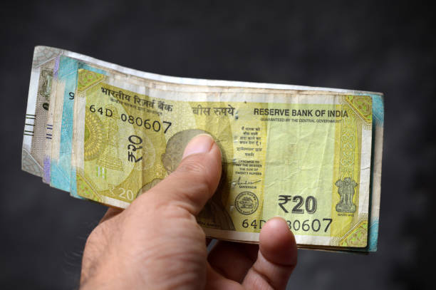 One hand holding stack or pile of Indian Rupees currency paper notes cash stack with various denominations and  20 rupees on top, showing off a bundle of money, over horizontal dark black background. Can be used as money lending, shopping, loans, payments, savings, investments, related backdrops with copy space.