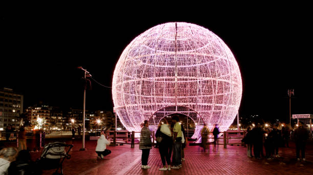 Las Palmas de Gran Canaria, Spain - December 30 2024: Tourists and locals enjoy a light installation in form of a Christmas bauble at La Puntilla square at the northern end of Las Canteras town beach