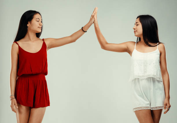 Two young filipino women celebrating success with a high five, radiating joy and excitement while dressed in casual summer outfits against a light gray background