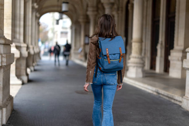 Rear view shot of female University student with backpack leaving college building after lectures