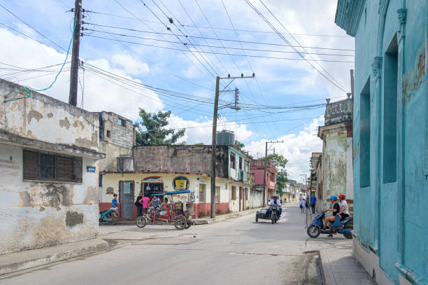 Santa Clara, Cuba - December 17, 2024: Weathered architecture of houses and diverse transportation vehicles on a city street