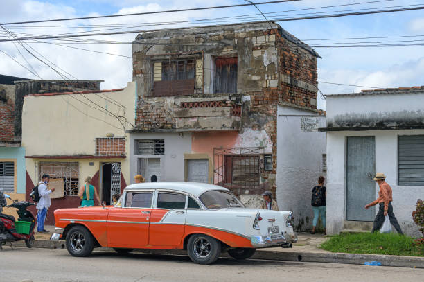 Santa Clara, Cuba - December 26, 2024: Cuban people are out and about a weathered house and a vintage Chevrolet car